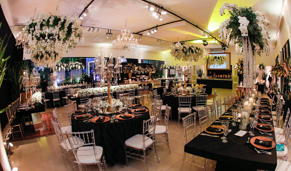 Mesas postas no salão, sob arranjos suspensos de flores brancas